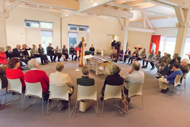 Gasten in een kring rond de overledene in een lichte zaal
