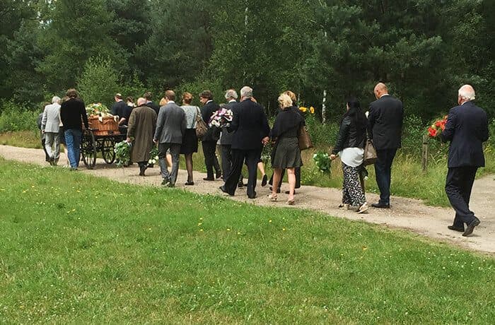 Rouwstoet over een bospad achter een baar met bloemen