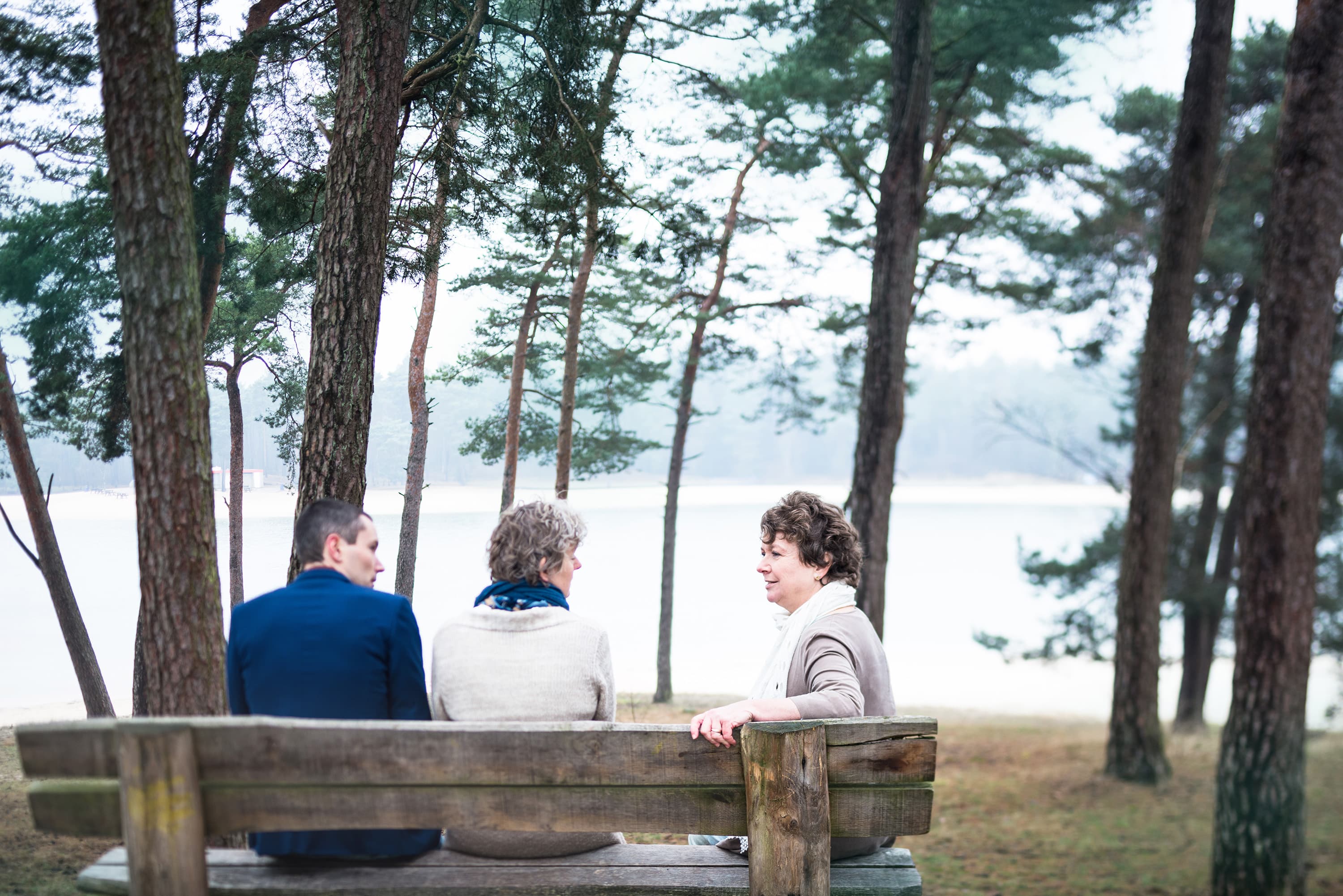 Drie mensen op een bankje tussen de dennen aan het meer